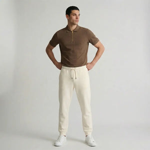 Man wearing a brown polo shirt and white pants against a plain background