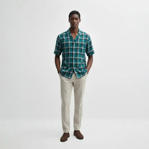 Man wearing a green plaid shirt and beige pants on a white background