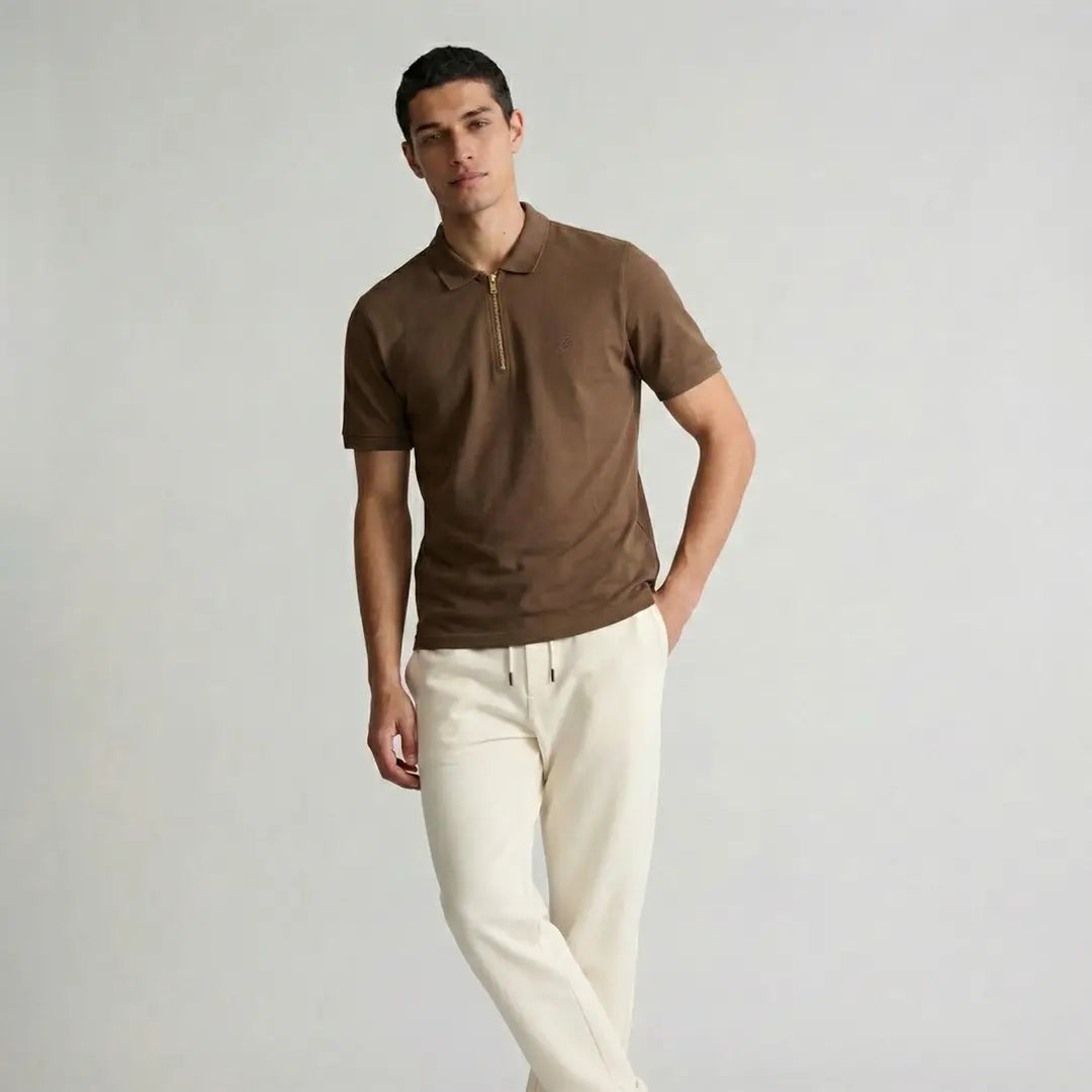 Man wearing a brown polo shirt and white pants against a plain background