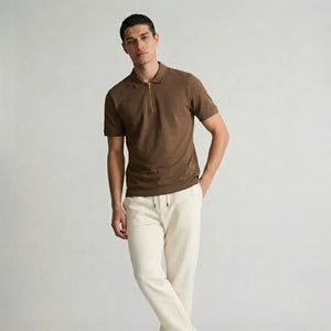 Man wearing a brown polo shirt and white pants against a plain background