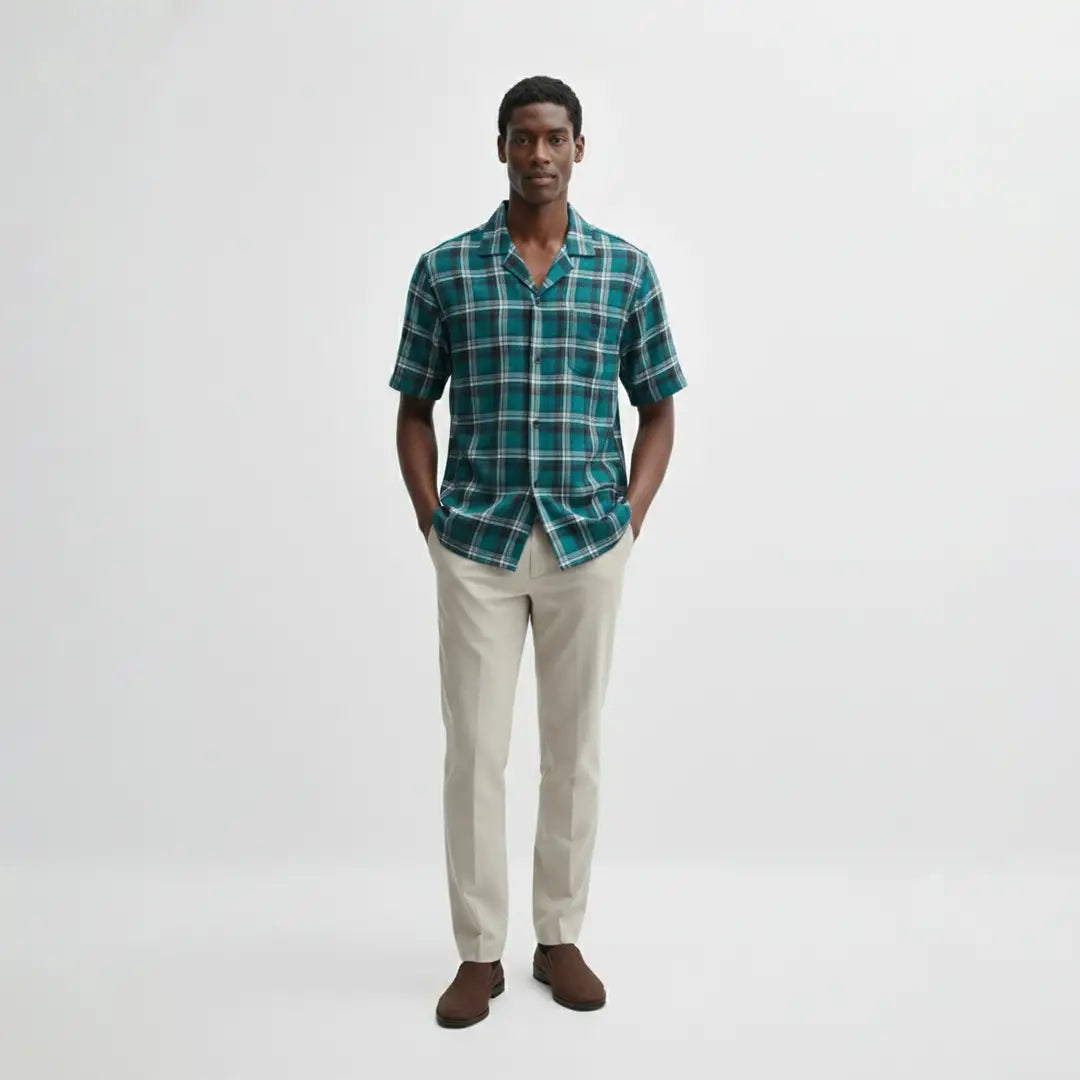 Man wearing a green plaid shirt and beige pants on a white background