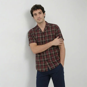 Man wearing a plaid shirt and dark pants against a plain background